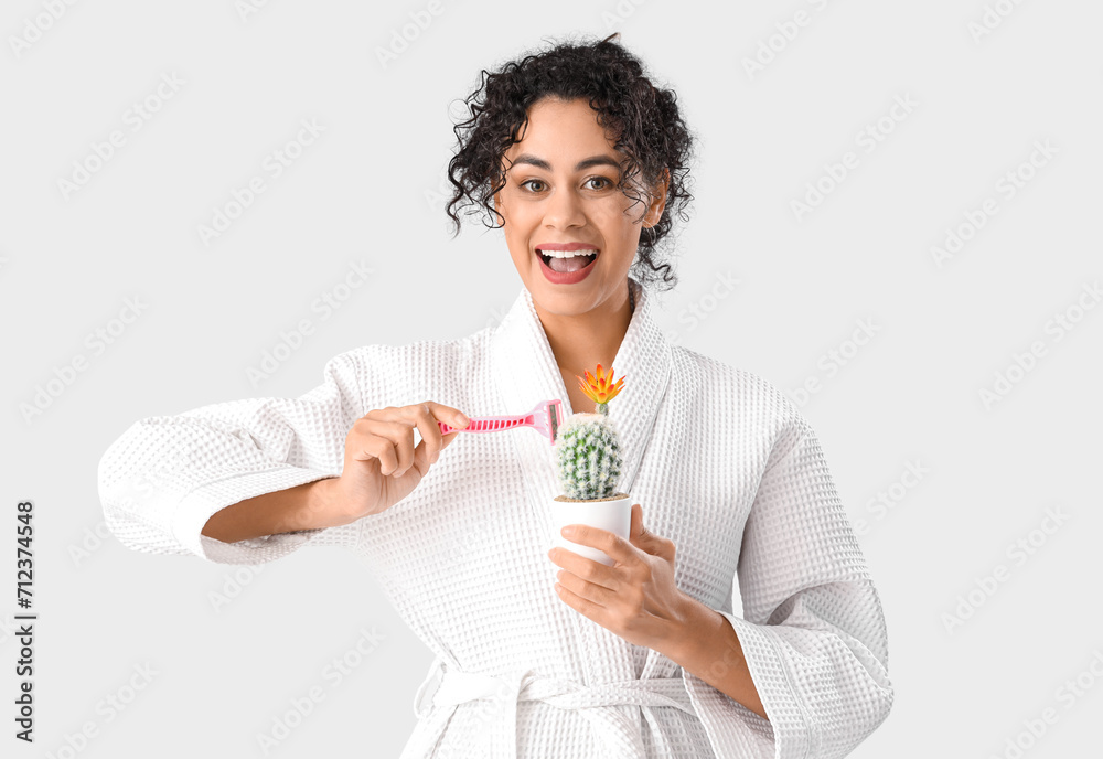 Beautiful African-American woman with razor and cactus on white background. Hair removal concept Beautiful African-American woman with razor and cactus on white background. Hair removal concept