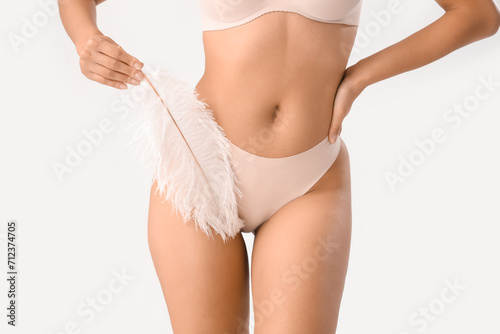 Beautiful young woman in underwear and with soft feather on white background. Hair removal concept photo