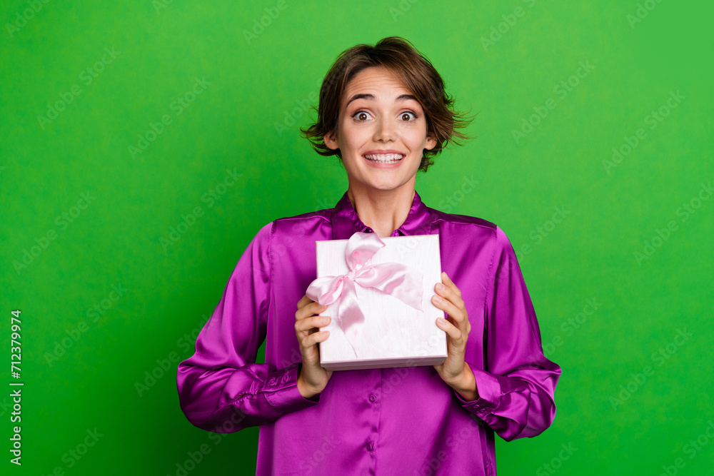 Portrait of excited toothy smiling girl in pink shirt holding wrapped gift box during working day isolated on green color background Portrait of excited toothy smiling girl in pink shirt holding wrapped gift box during working day isolated on green color background