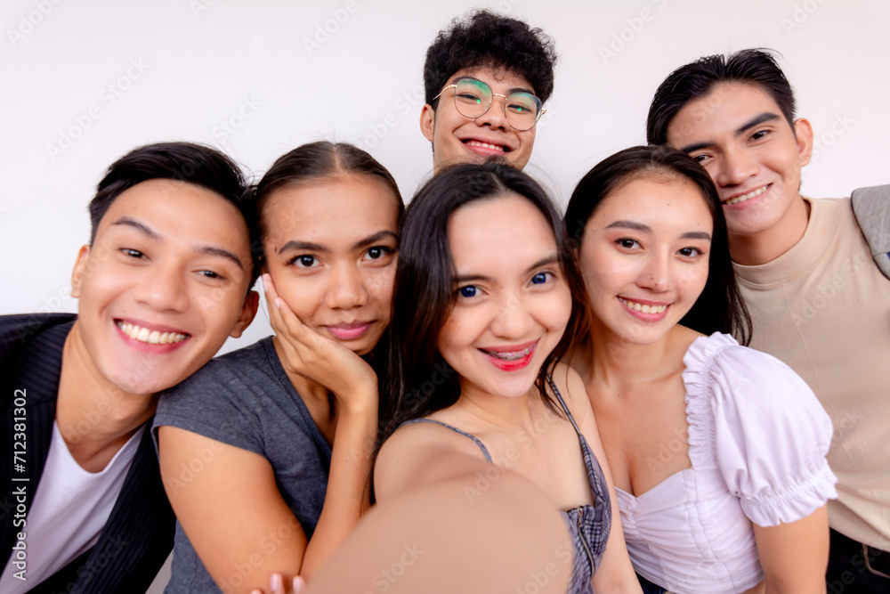 A diverse group of six happy young friends taking a group selfie with a smartphone, smiling and enjoying togetherness.