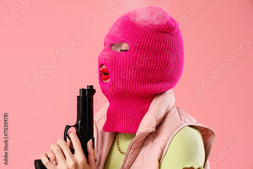 Beautiful young stylish woman in balaclava with gun on pink background photo