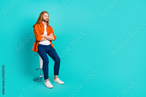 Full size photo of confident guy wear stylish outfit sit on stool look at proposition empty space isolated on turquoise color background