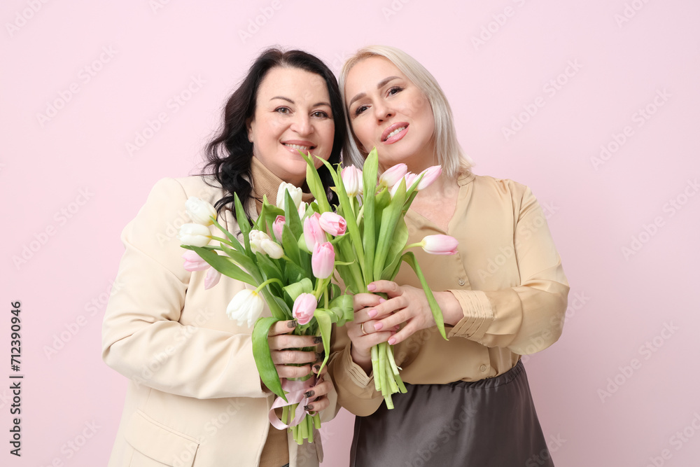 Mature women with bouquets of beautiful tulips on pink background. International Women's Day Mature women with bouquets of beautiful tulips on pink background. International Women's Day
