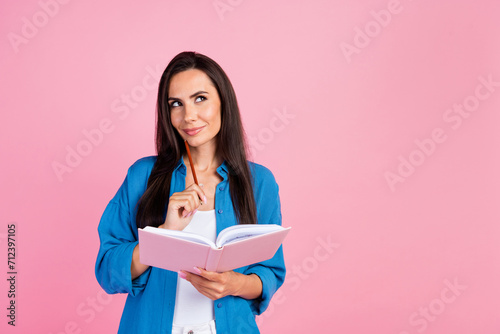 Photo of minded girl with straight hair dressed blue shirt hold notebook pencil on chin look empty space isolated on pink color background