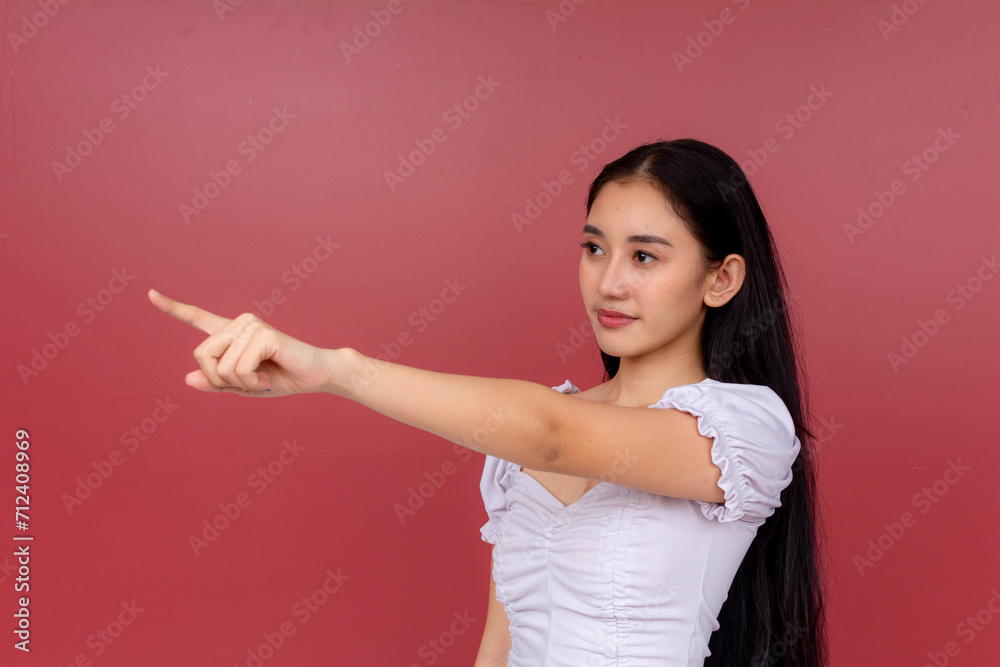 Elegant Asian woman in a white blouse pointing to the side against a red backdrop, showing direction and focus. Elegant Asian woman in a white blouse pointing to the side against a red backdrop, showing direction and focus.