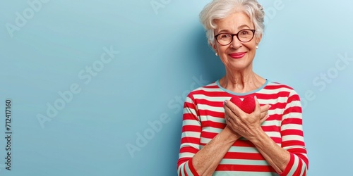 An elegant, fit granny with a charming smile, wearing glasses, holds a red apple in the kitchen.