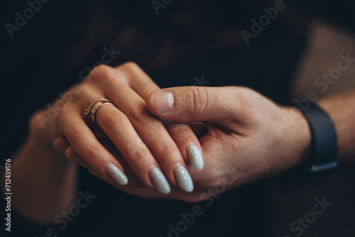 A strong male hand holds a gentle female hand with two gold rings on the finger. Low key. Dark, blurry background.