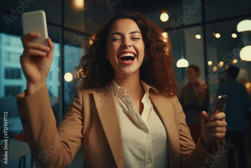 Euphoric young female worker holding mobile phone celebrating win receiving good news about job promotion, getting hired, feeling happy, rejoicing success with yes reaction working in office. Vertical