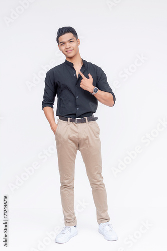 Stylish young Filipino man posing on a white background, exuding confidence and trendy casual style. Pointing to himself.