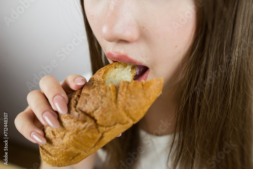 young beautiful girl eating a croissant  close-up  crop photo. female mouth eating croissant