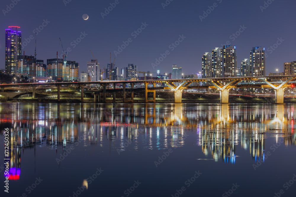 The moon, bridge and buildings are reflecting on the Han river ripples in Seoul.