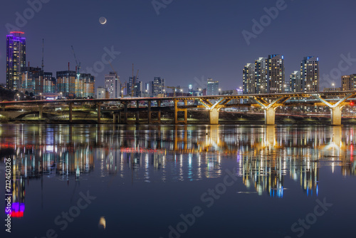 The moon, bridge and buildings are reflecting on the Han river ripples in Seoul. © Sepe44