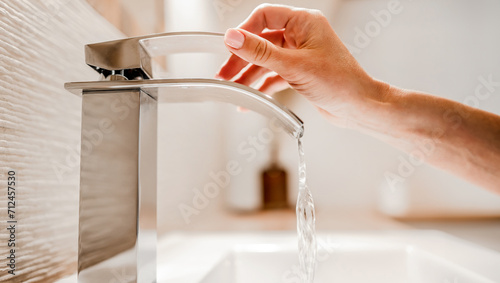 Girl hand open water from steel faucet in bathroom. Woman using silver tap at home for cleaning and hygiene