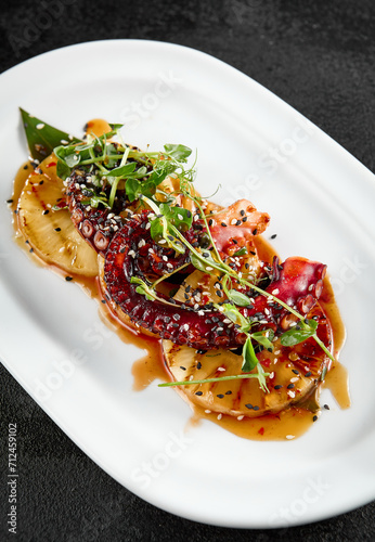Grilled pineapple rings and tender octopus garnished with green herbs, served on a white elongated plate