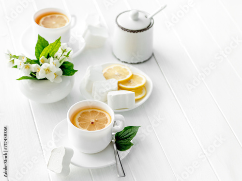 Cups of green herbal tea, jasmine flowers, sweets and cubes of sugar, lemon cut