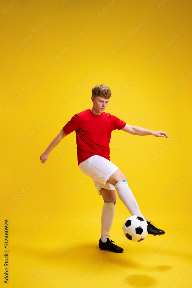 Obraz premium Young man in sportswear, uniform playing football, dribbling soccer ball against yellow studio background. Training. Concept of active lifestyle, youth, hobby and human emotions