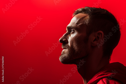 A man expressing determination and resilience, his focused gaze against a powerful red monochrome background. photo