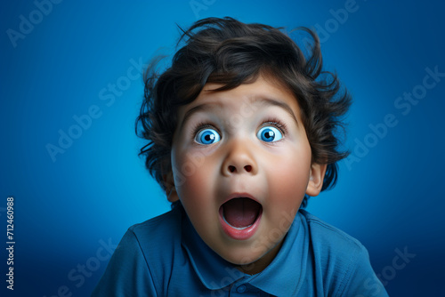 An adorable child with a surprised expression, eyes widened in innocent wonder, against a dynamic blue monochrome background. photo