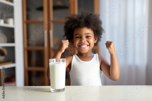 Milk, portrait and African girl with muscle from healthy drink for energy, growth and nutrition in the kitchen. Happy, smile and child flexing muscles from calcium in a glass and care for health  photo
