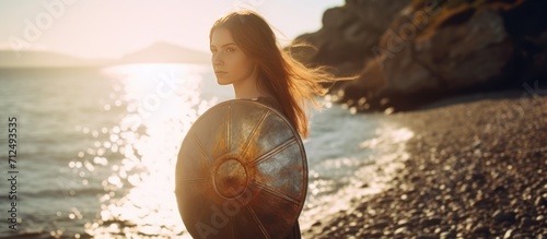 Young woman stands carrying a shield