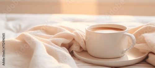 Coffee cup on a white blanket on a bed with blurred foreground and background.
