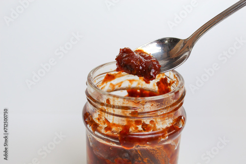 Sambal is an Indonesian chilli sauce or paste. On a silver spoon, taken from a transparent glass jar. Isolated on white background photo