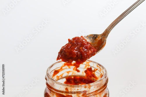 Sambal is an Indonesian chilli sauce or paste. On a silver spoon, taken from a transparent glass jar. Isolated on white background