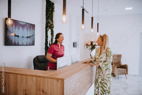 A beautiful blonde woman conversing with the dental clinic receptionist, scheduling an appointment for dental treatment with a bright smile photo