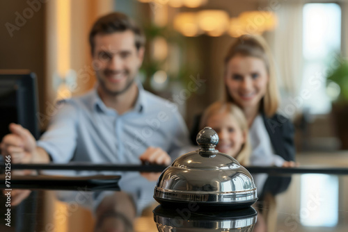 Closeup photo of bell for staff at hotel reception desks and happy family defocused in background. Family travel or hotel check-in concept