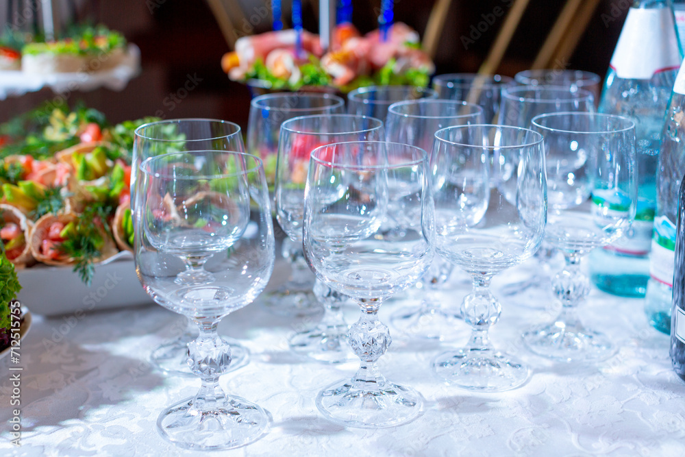 A group of crystal wine glasses on a white tablecloth against the background of a festive table with appetizers with red fish, avocado and herbs