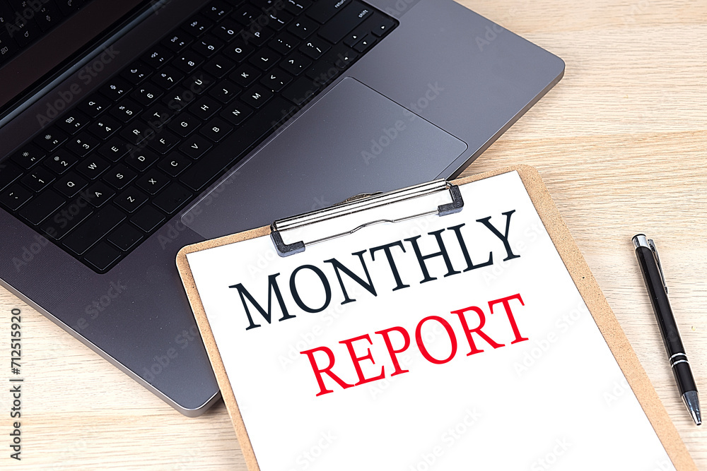MONTHLY REPORT text written on a paper clipboard on laptop