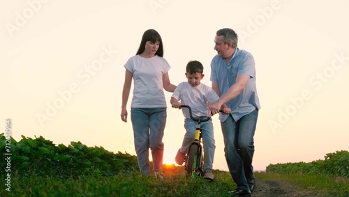 Parents educate son in cycling during summer holiday. Boy acquires skill of cycling with assistance of parents during summer break. Son shares moments with parents mastering art of cycling at sunset