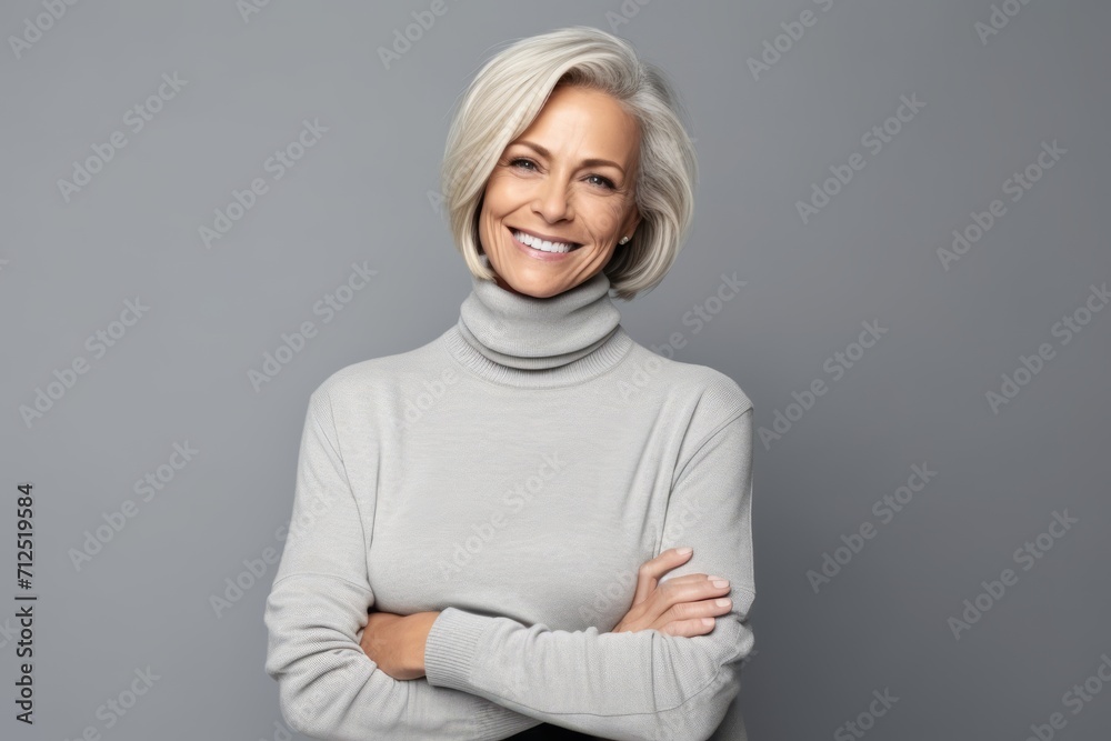 smiling senior woman in grey sweater with crossed arms over grey background smiling senior woman in grey sweater with crossed arms over grey background