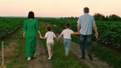 Mother father and sons stroll through plantation in evening. Sons spend time with mother and father on weekend after sunset. Father mother and children walk around vegetable garden on vocation