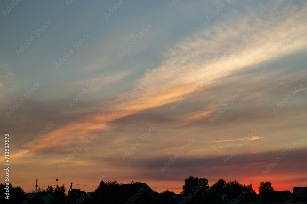 Beautiful evening sky at sunset over silhouettes of houses. Summer landscape.