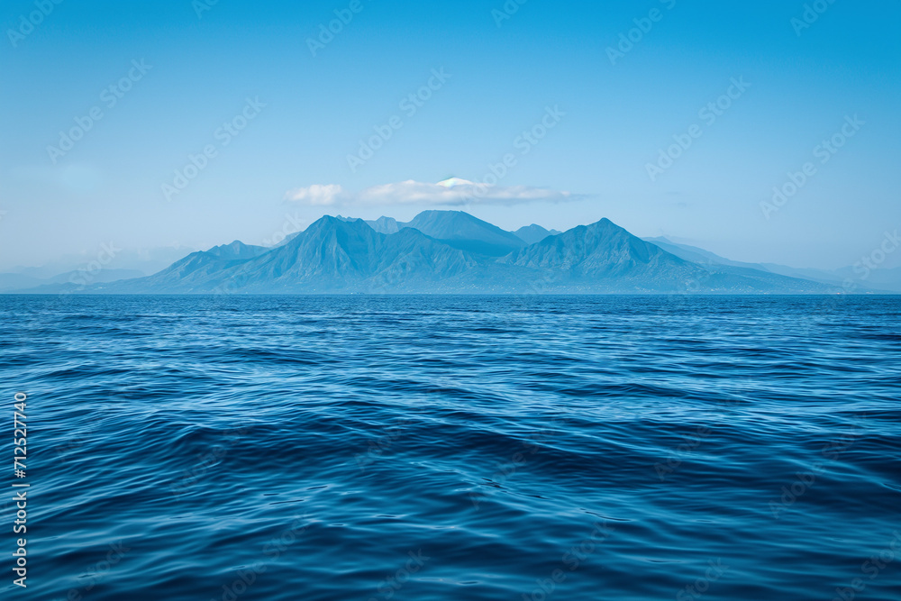 The image shows a mountain range in the middle of the ocean. The mountains are tall and jagged, and they rise from the deep blue water.