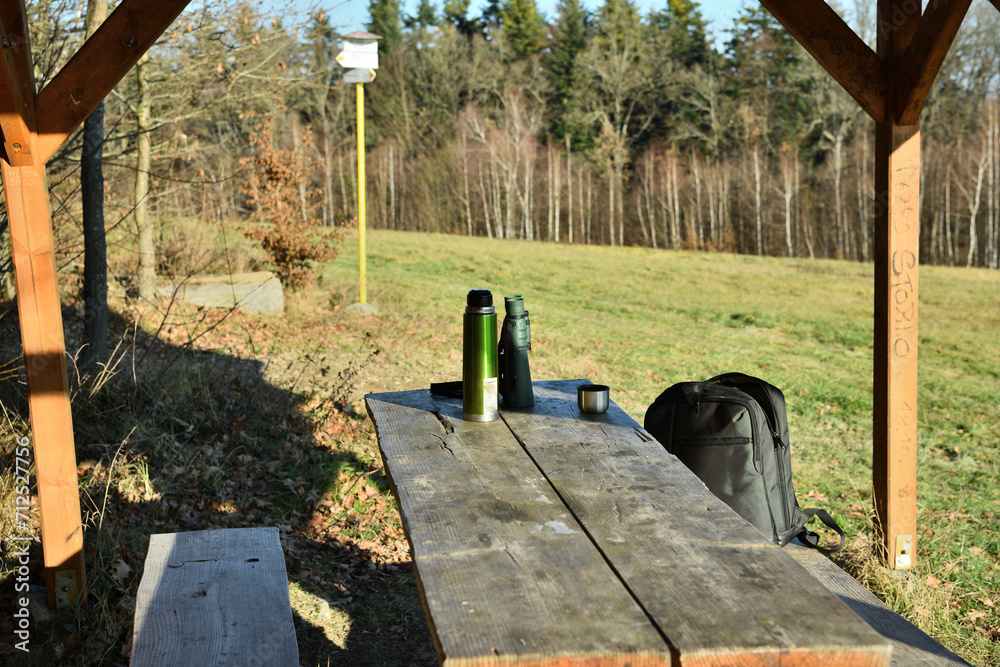 Tourist bench relaxing in the woods on the table with a thermos for coffee, binoculars and a backpack