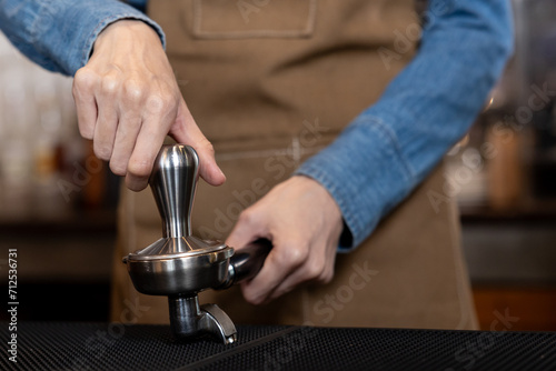 White Asian woman's hand Press the ground coffee tamper to make a close-up of espresso. Put on an apron