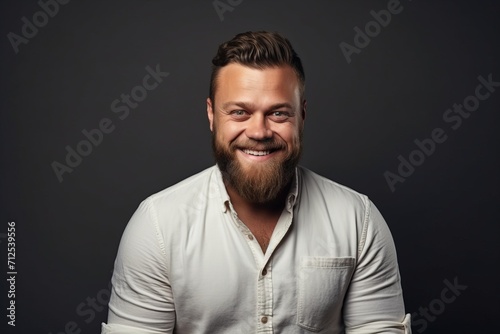 Portrait of a smiling bearded man in a white shirt over dark background.