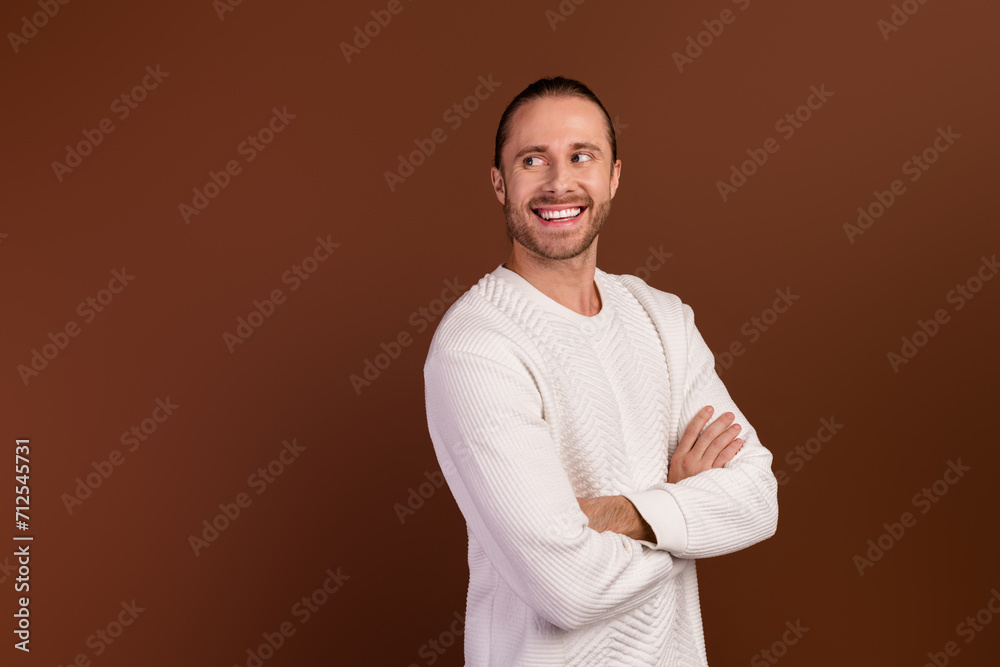 Photo of good mood dreamy guy dressed white pullover arms folded looking back empty space isolated brown color background Photo of good mood dreamy guy dressed white pullover arms folded looking back empty space isolated brown color background