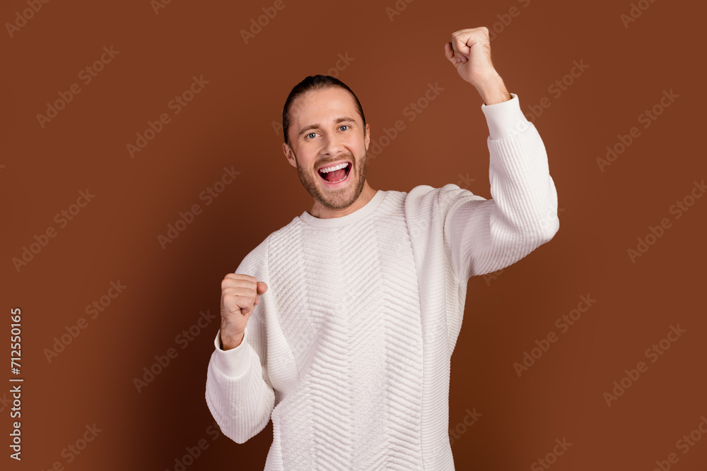 Photo of excited lucky guy dressed white pullover screaming yeah rising fists isolated brown color background