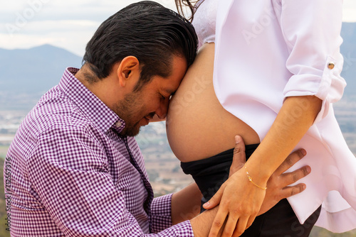 An intimate close up of man kissing the exposed belly of his seven month pregnant partner expressing lovewith a scenic view of Tequisquiapan Mexico in the background photo