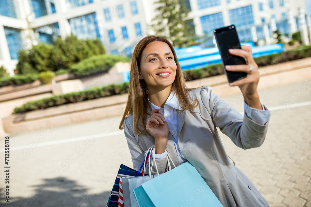 Fototapeta premium Attractive young woman taking picture on her cellphone outside while shopping in the city