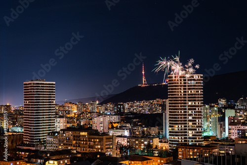 A vibrant display of fireworks bursting over the night sky of Tbilisi, lighting up the cityscape with various colors and patterns photo