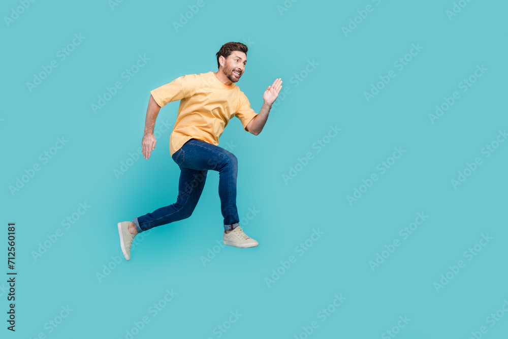 Full body size photo of sportive man in yellow t shirt and denim jeans running air to his target isolated on aquamarine color background Full body size photo of sportive man in yellow t shirt and denim jeans running air to his target isolated on aquamarine color background
