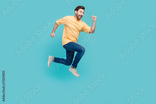 Full body size photo of funky young brunet man in yellow t shirt and jeans jumping run to his dream isolated on blue color background