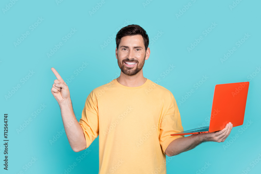 Photo of young brunet man wearing yellow t shirt recommend it courses for beginners holding computer isolated on cyan color background Photo of young brunet man wearing yellow t shirt recommend it courses for beginners holding computer isolated on cyan color background