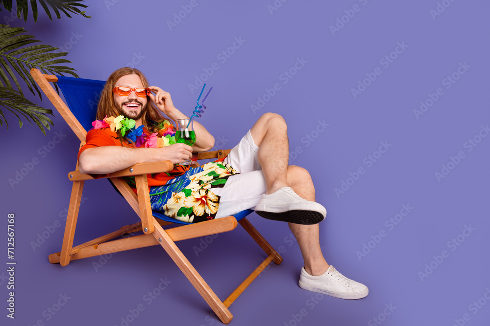 Full size photo of funny positive man touch sunglass sit on armchair with cocktail at ocean beach isolated on purple color background Full size photo of funny positive man touch sunglass sit on armchair with cocktail at ocean beach isolated on purple color background
