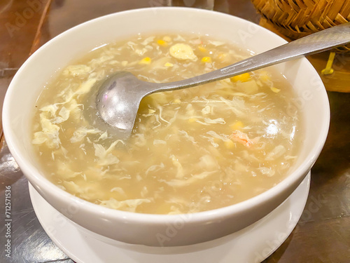 Egg drop soup with crab meat in white porcelain bowl on wooden table. Egg flower soup is a thick Chinese soup of wispy beaten eggs in chicken broth.