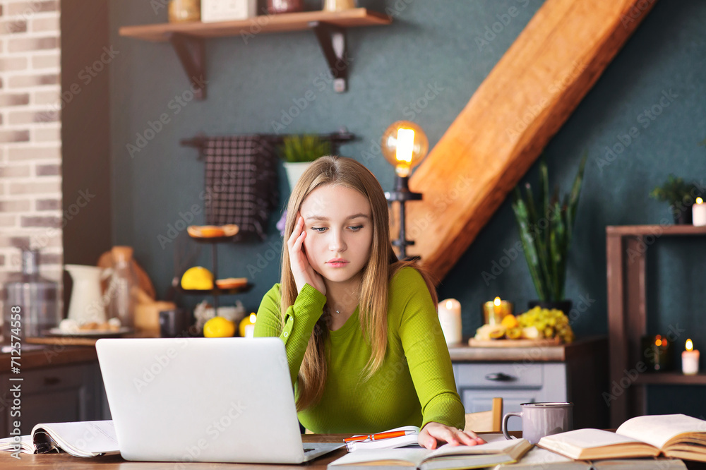 Young pensive woman freelancer sitting at table at home with laptop, making notes Young pensive woman freelancer sitting at table at home with laptop, making notes